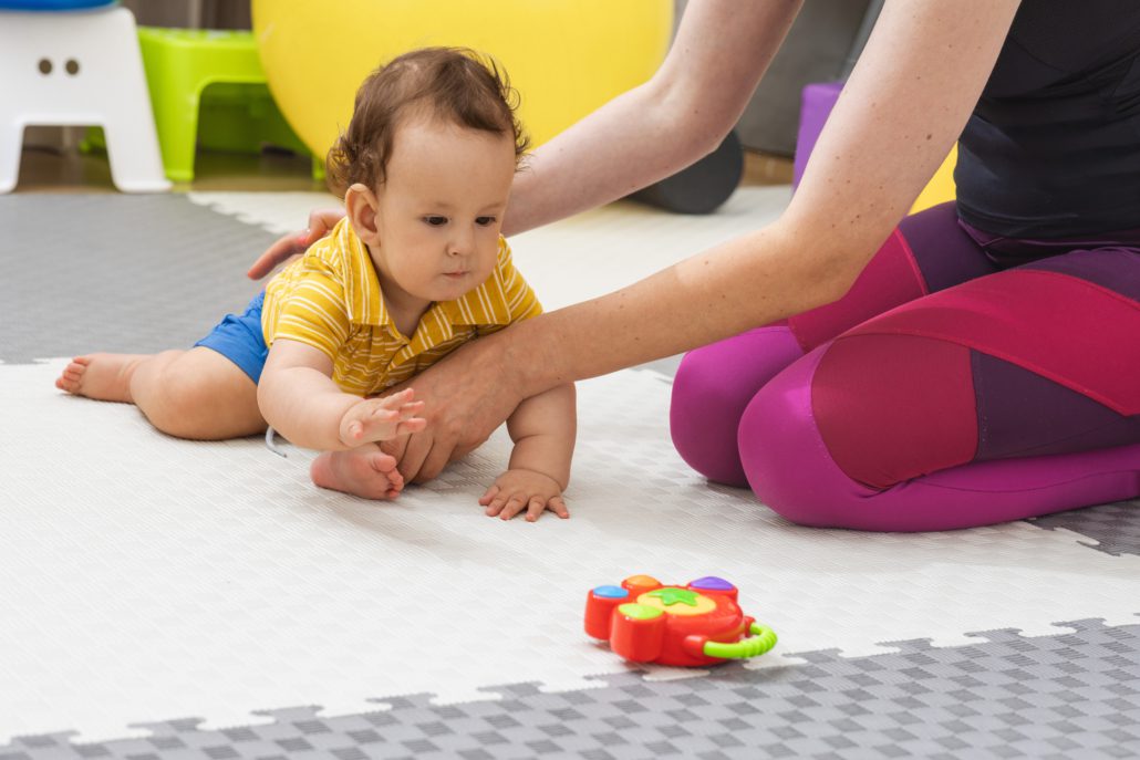 Physical therapist helps a baby crawl towards a toy during a physiotherapy session