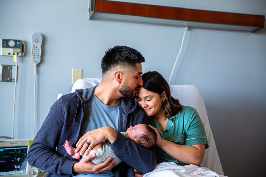 Mother and father in hospital bed holding newborn baby.